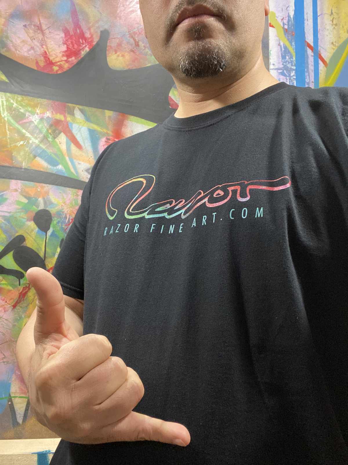 Figure wearing graffiti fill logo t shirt with the hang loose gesture.