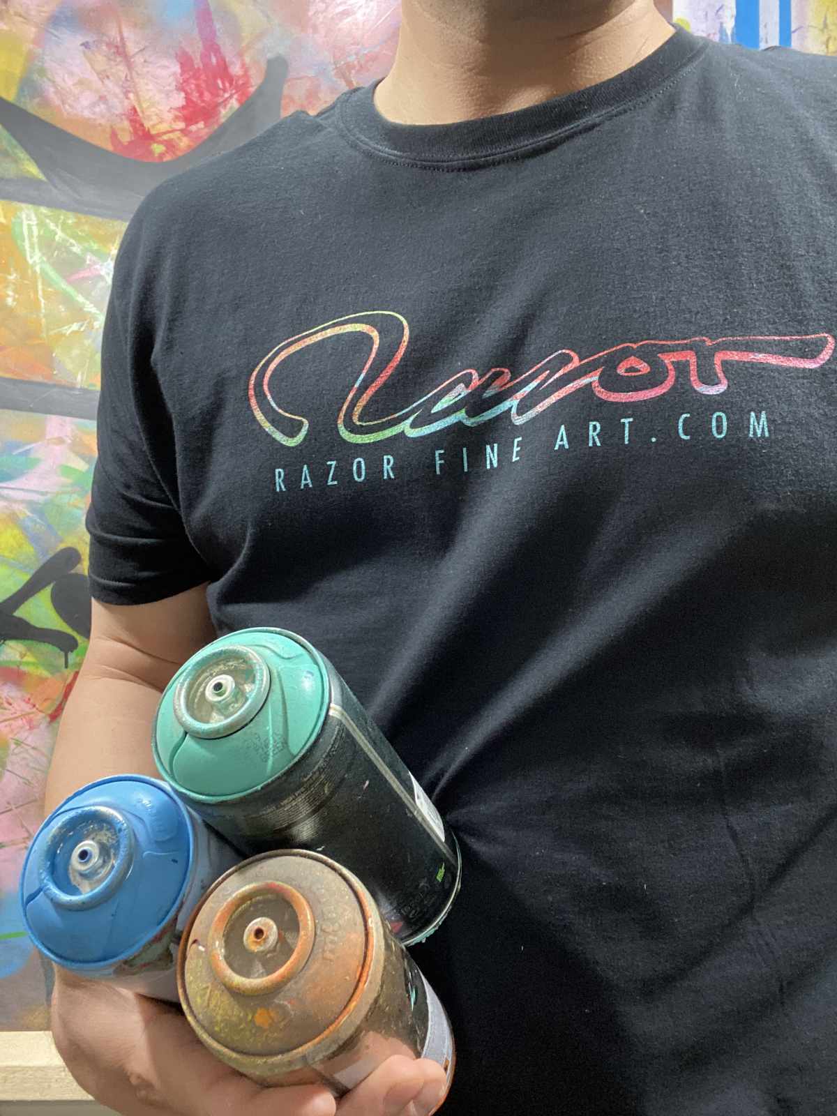 Figure wearing logo t shirt holding spray paint cans.
