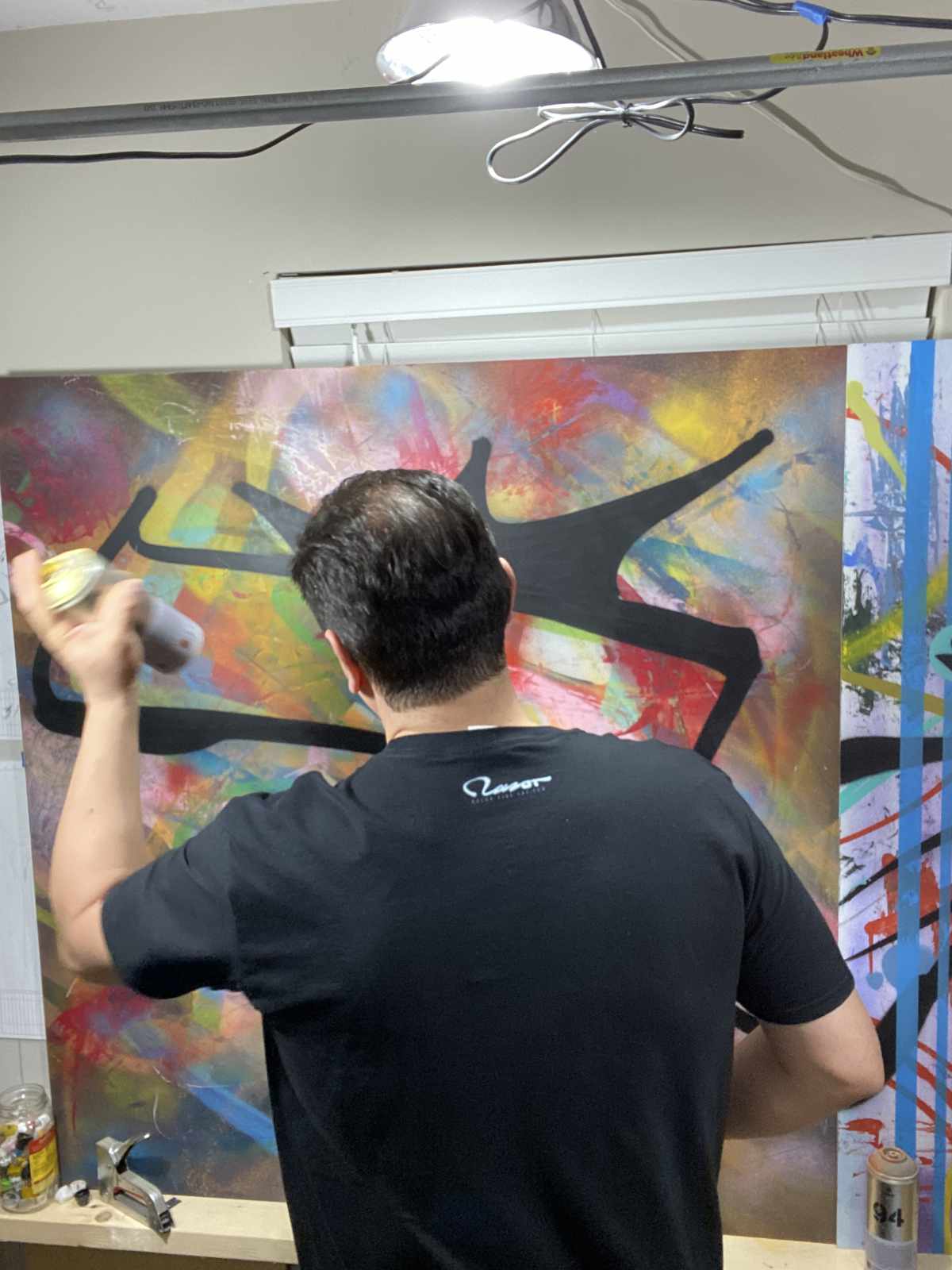 Figure wearing t shirt with upper back logo hit spray painting in the studio.